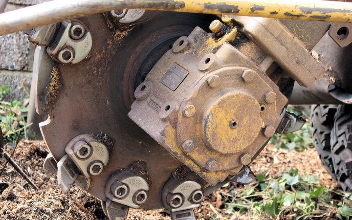Close-up of a stump grinder cutting wheel and its teeth over wood chips